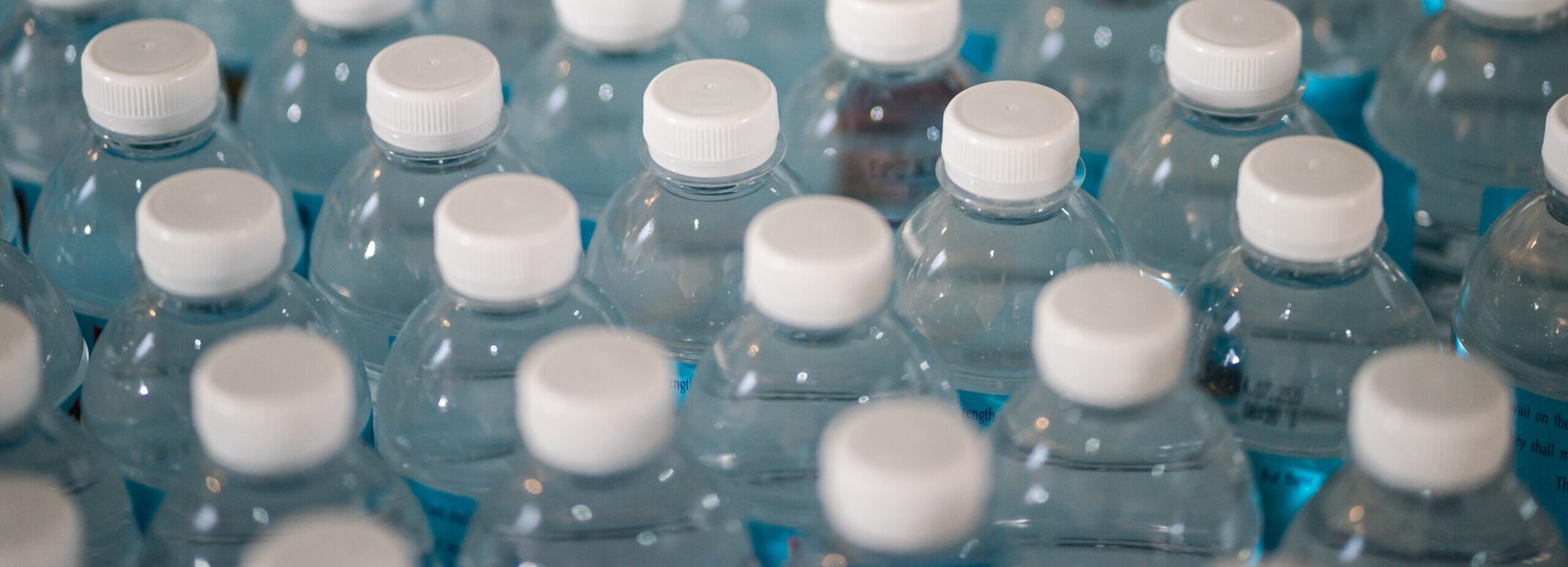 Rows of plastic water bottles are viewed from above. What are the consequences of the policies that govern their manufacture, use, and disposal?