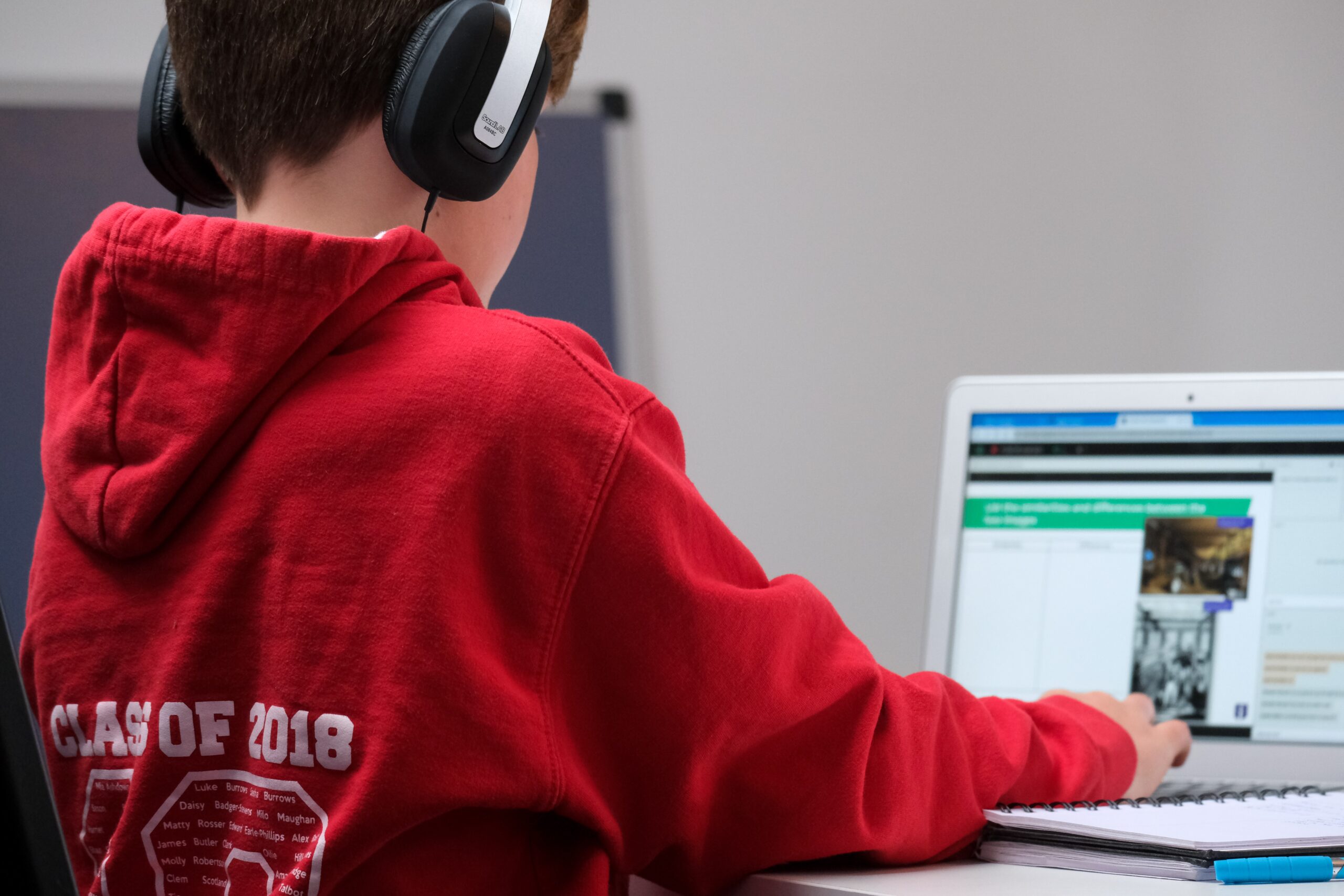 boy in red hoodie wearing black headphones sitting in front of a laptop