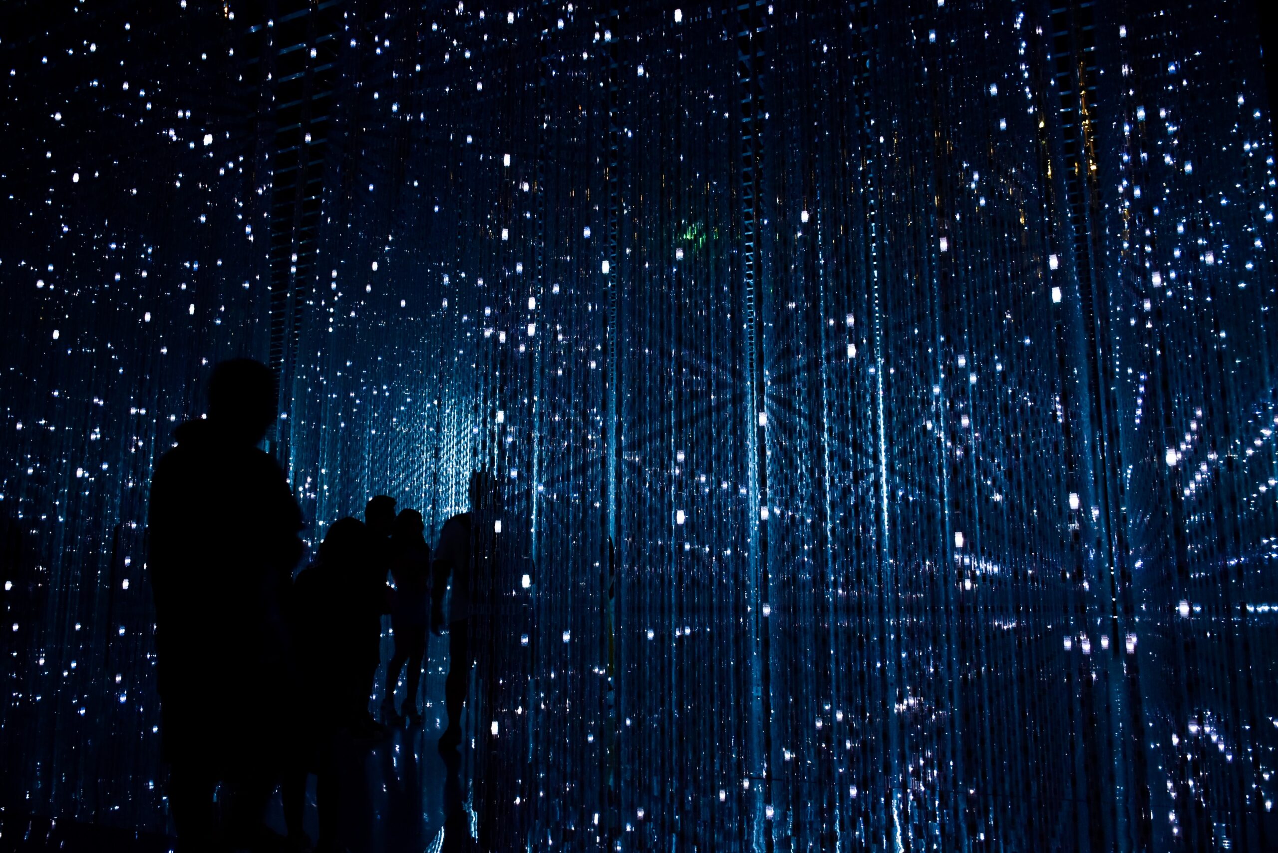 Silhouettes of several people stand in the foreground, surrounded and overlaid by futuristic white lights and grid-like blue lines that call to mind a digital space.