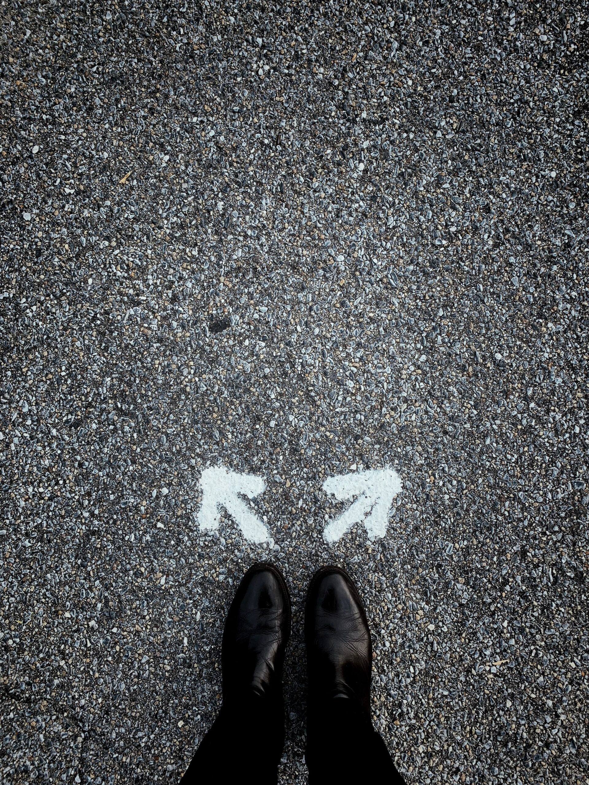 A person standing in the middle of the street, white arrows pointing in opposite directions in front of their feet.