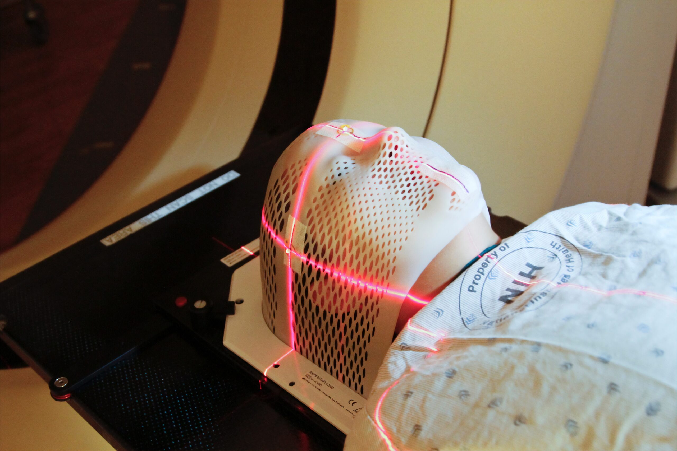 Person laying inside an MRI machine and wearing a mask covering their face. Lasers pass over their head and face.